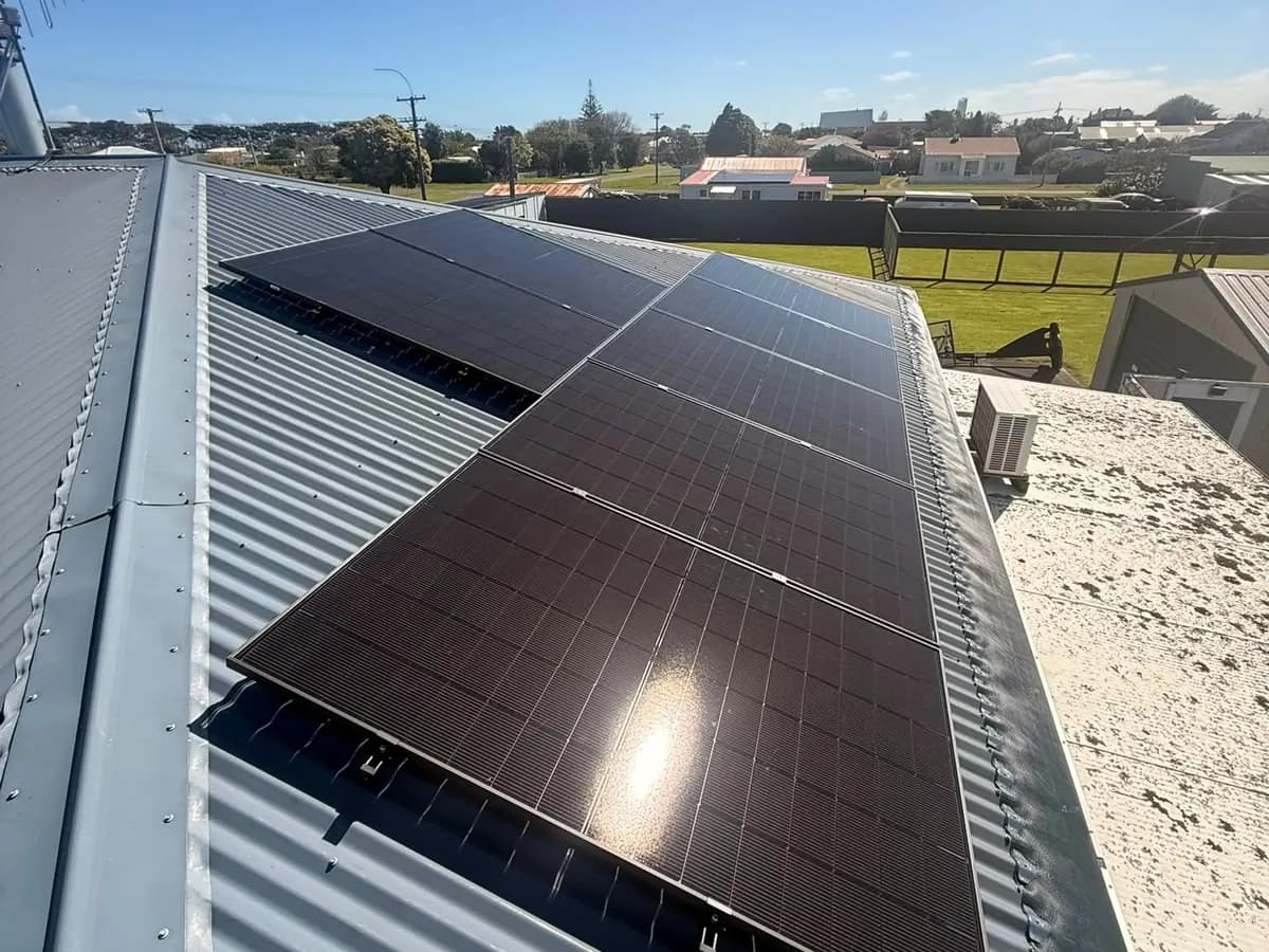 A 6.83kW EFS Solar array on a grey metal roof at Manaia, Taranaki, with a rural sports ground behind