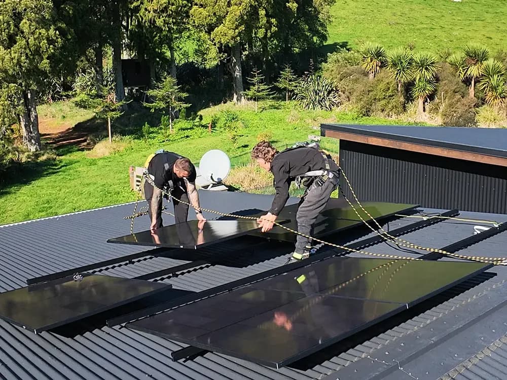 Two EFS Solar installers laying panels on a rural Raglan roof, Waikato hill country behind