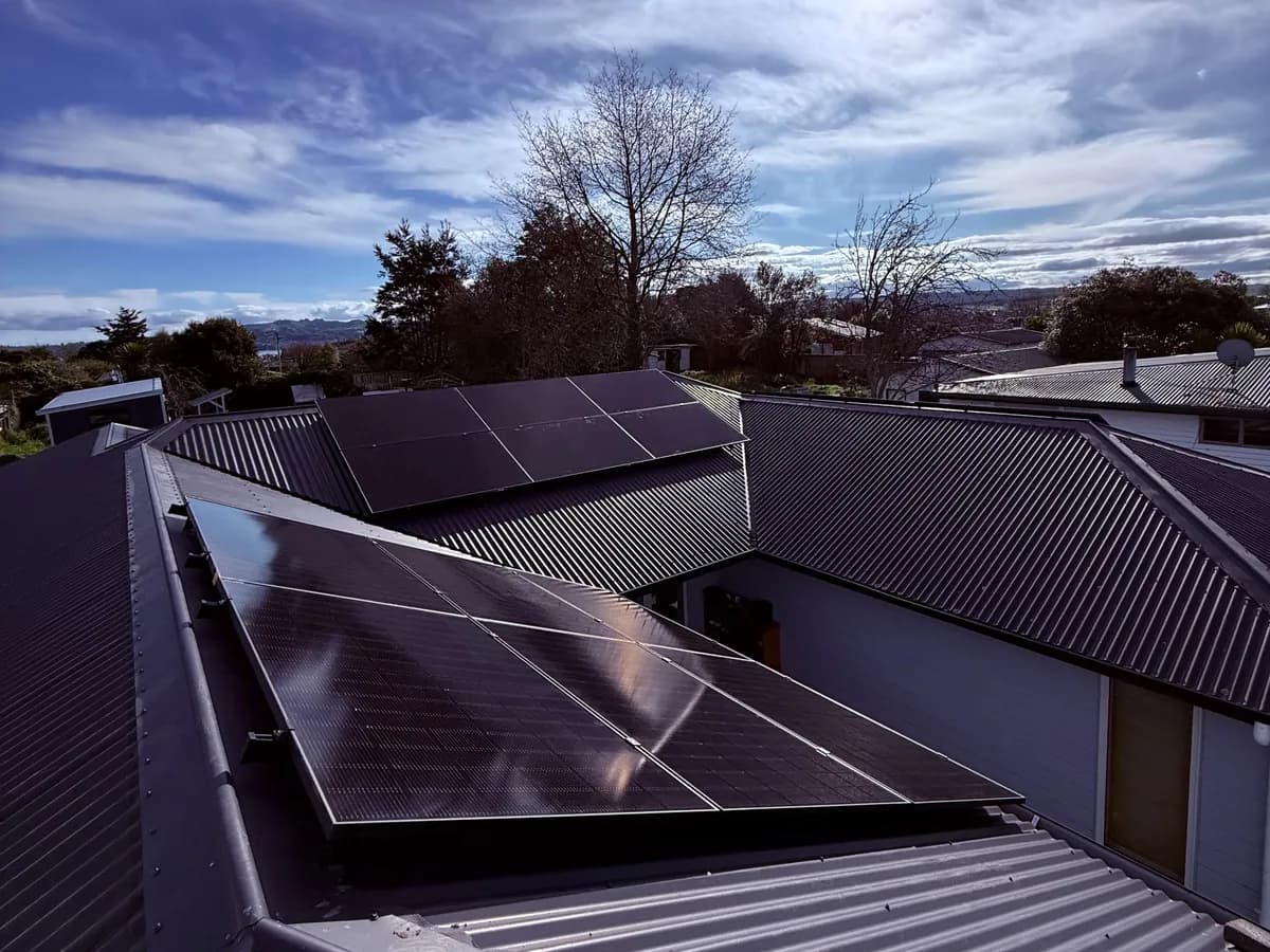 A 9kW EFS Solar array on a charcoal metal roof in Taupō, Waikato, with a hilltop view behind
