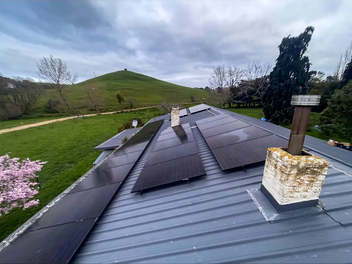 A 13.65kW EFS Solar array on a charcoal metal roof at a rural Waiterimu property, Waikato, with a hill and magnolia behind